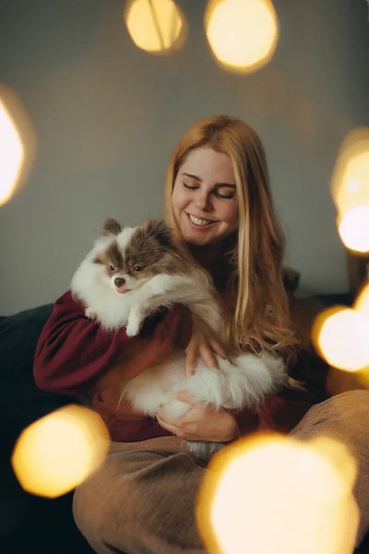 A smiling woman holding her fluffy dog at home, warm ambient lighting